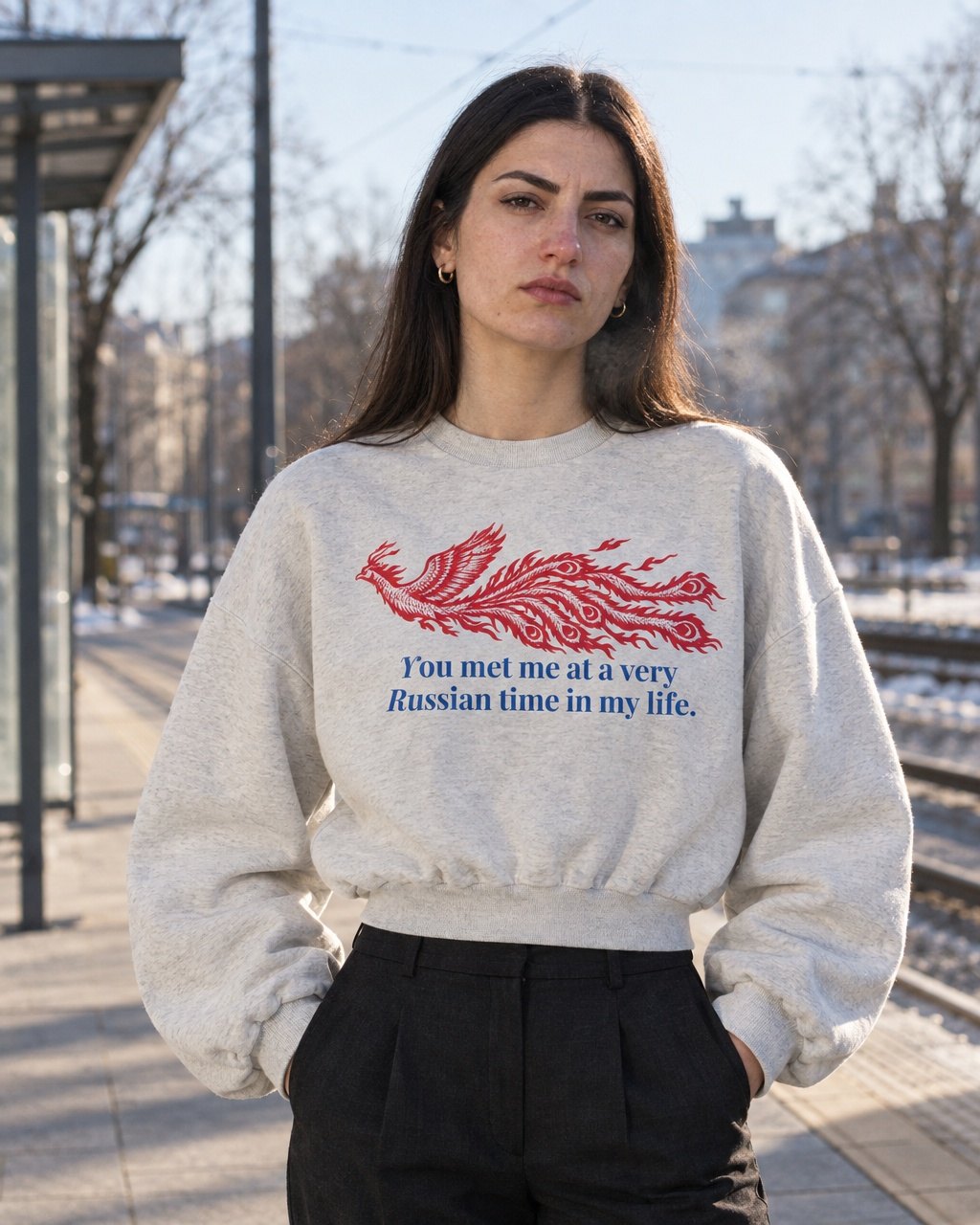 Frau am Bahnsteig im Winter, im oat-grauen Cropped Sweater mit rotem Feuervogel und dem Spruch you met me at a very Russian time in my life