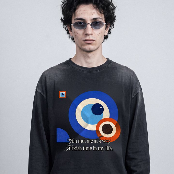 Junger Mann mit ovaler Sonnenbrille im sun-faded schwarzen Longsleeve mit Bauhaus-Nazar-Print