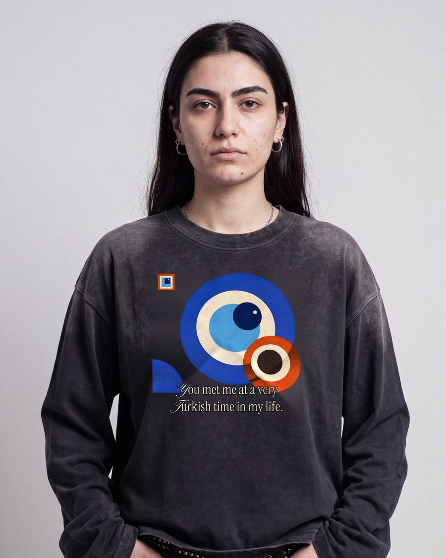 Junge Frau vor grauer Studiowand im sun-faded schwarzen Longsleeve mit Bauhaus-Nazar-Print